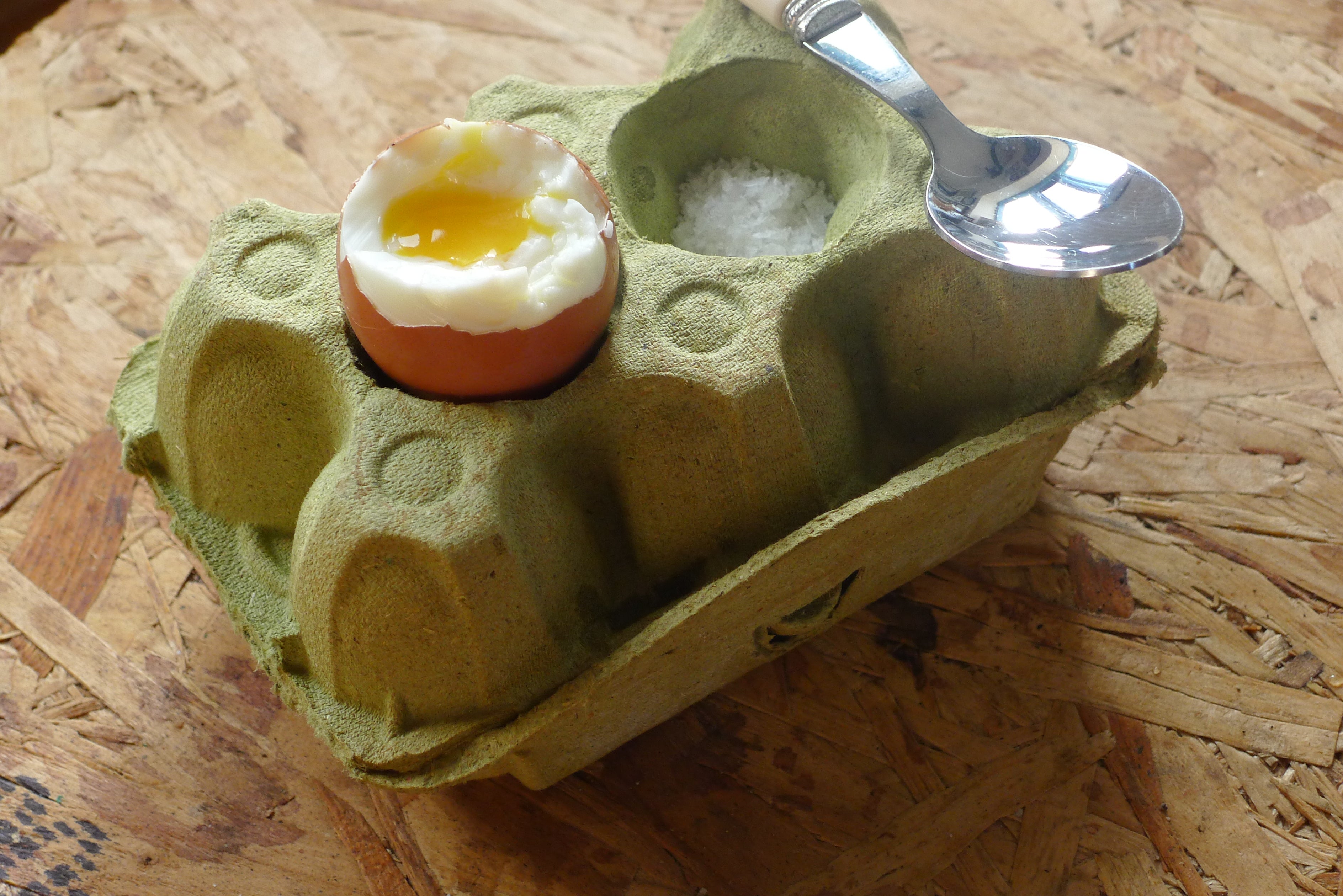 Boiled egg in a green egg carton with a spoon on a wooden surface